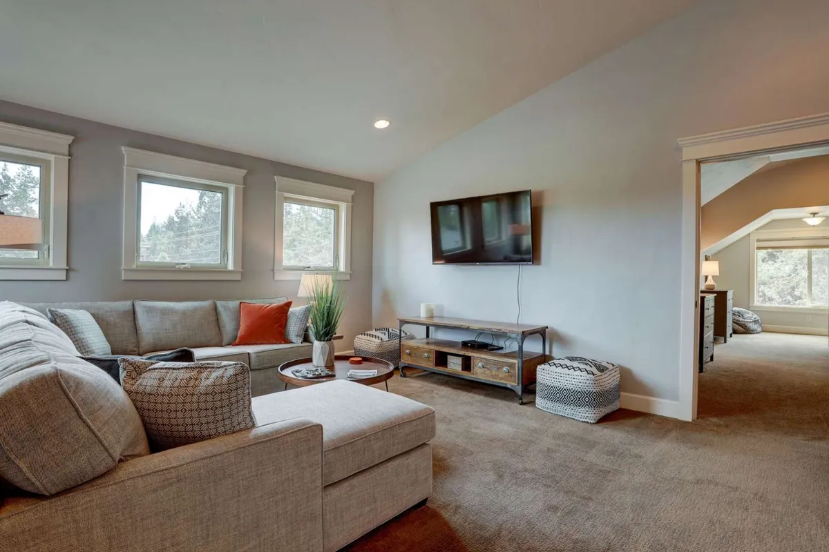 A comfortable media lounge with a sofa, TV, decorative plant, coffee table, and textured poufs, arranged in a way that encourages lounging, movie watching, and playing games.