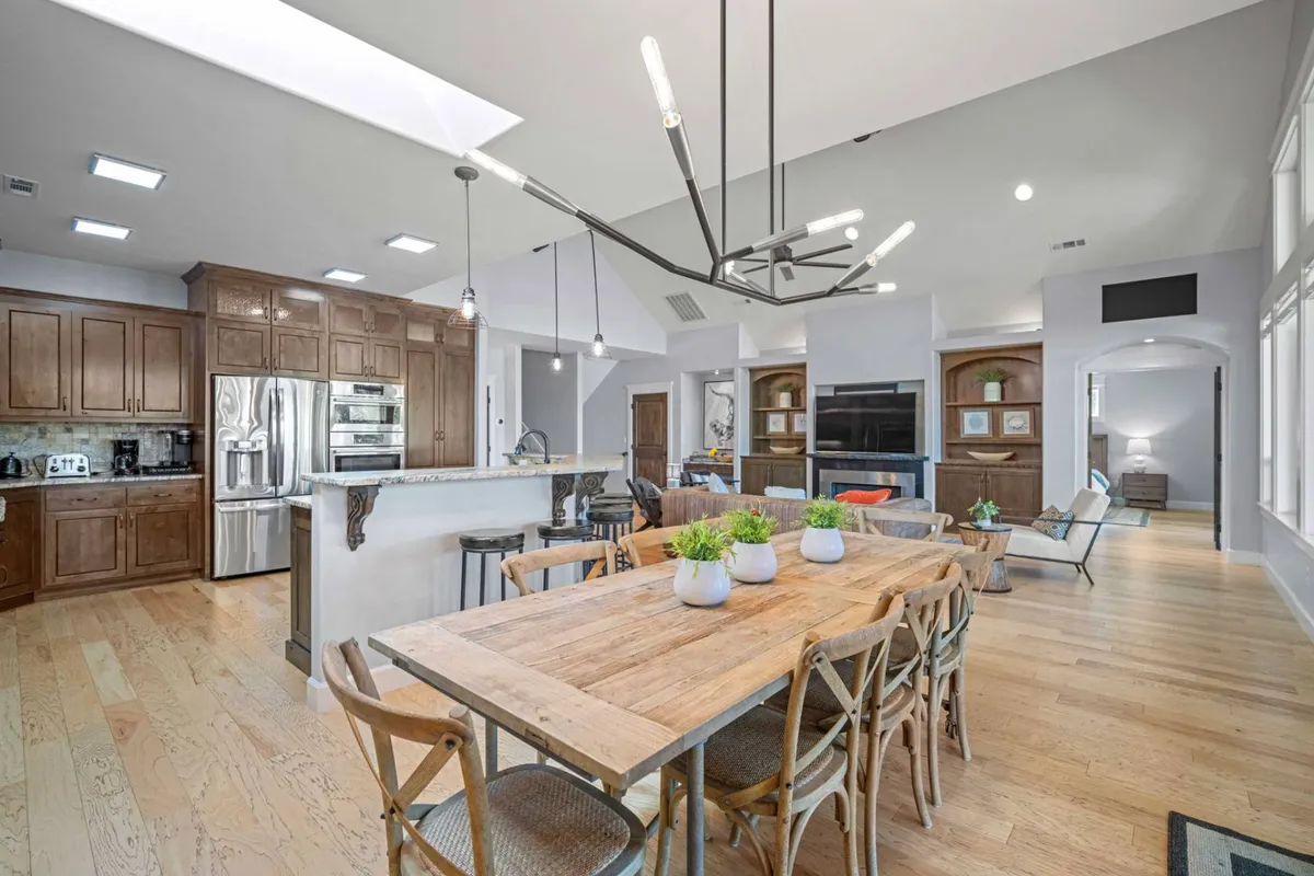 An inviting interior view featuring a large dining table, modern light fixture, kitchen area, and living room seating. The open-concept setting is stylish and designed for gatherings, perfect for shared meals, celebrations, and socializing, all with a sense of togetherness and warmth.