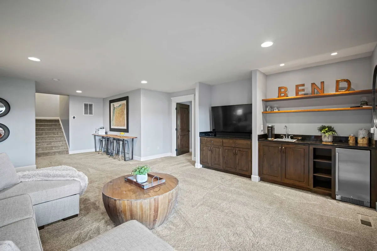 A welcoming family/media lounge with a comfortable sofa, coffee table, bar area, TV, and a decorative sign. The atmosphere is perfect for relaxing, watching movies, or socializing during a group stay.