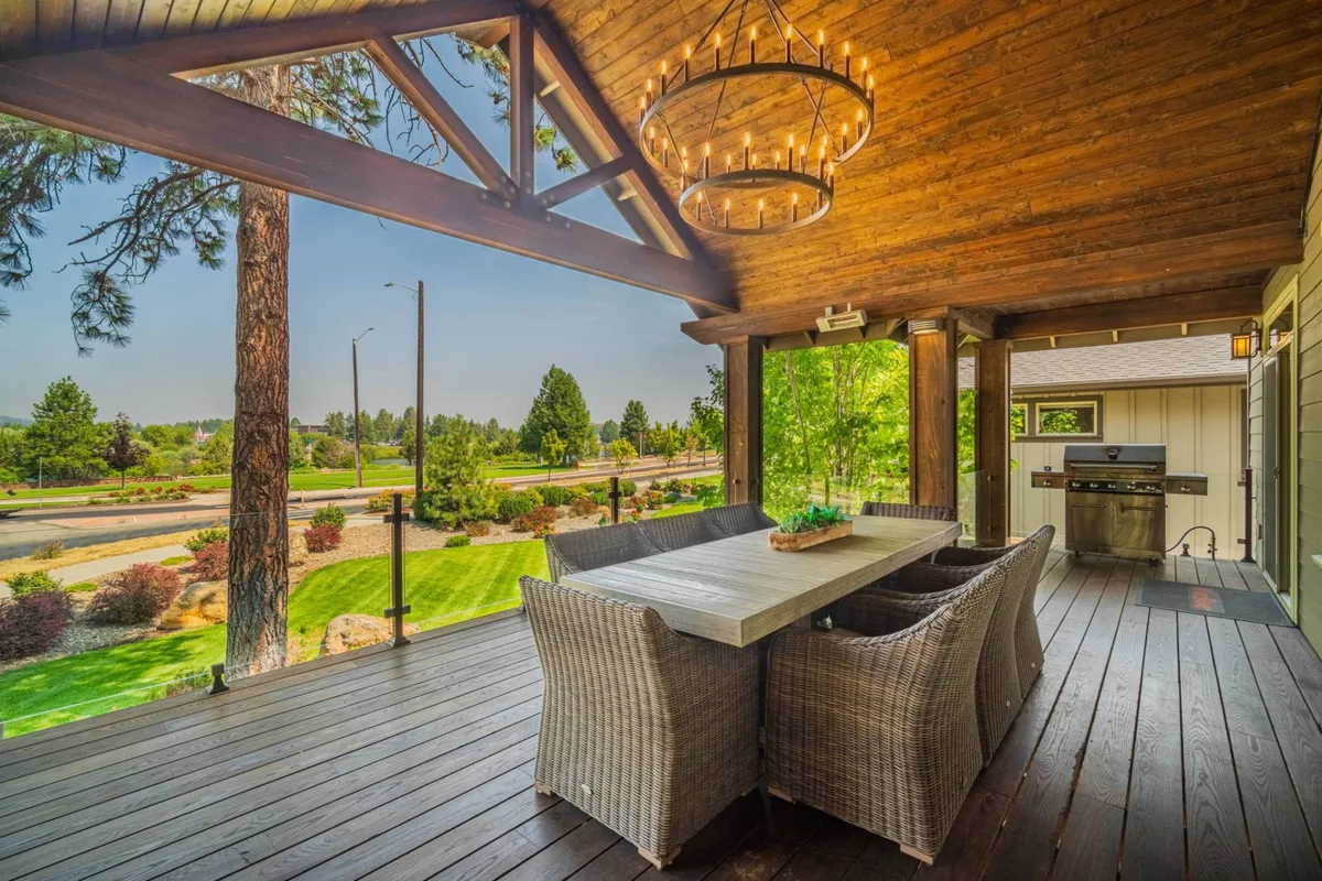 The main deck is featured here with a large outdoor dining table, woven chairs, a chandelier, and surrounding greenery. The deck exudes a welcoming and serene vibe, ideal for outdoor meals and gatherings, with hints of sunset light adding warmth.