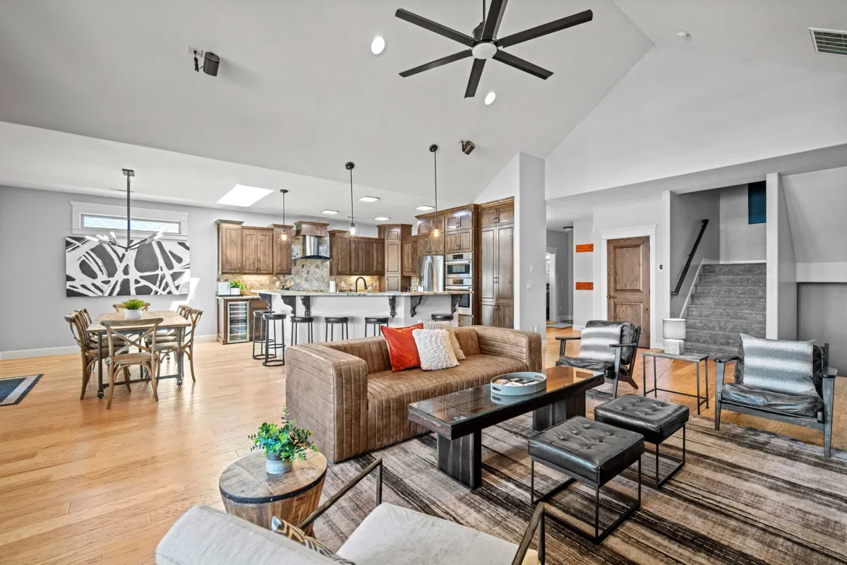 This image features a comfortable and stylish open-concept living area, including a sofa with red accents, a dining table, and a kitchen island with artwork visible on the wall. The scene suggests both warmth and sophistication, with ample space for socializing and relaxing, and the visible art pieces support the section's mention of original artwork.