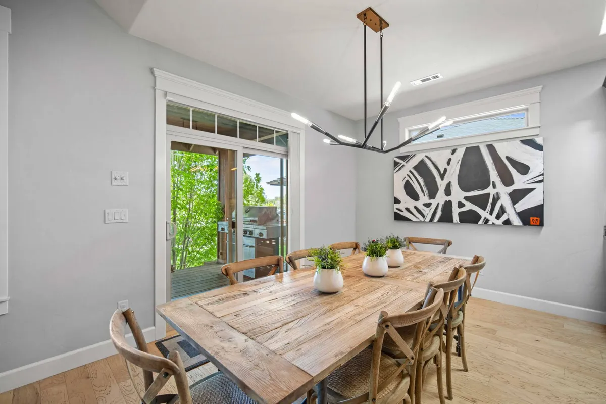 A warm dining area with a dining table, artistic lighting, wall art, and a sliding door leading directly to a deck. The space is ideal for family meals and entertaining, with direct access to outdoor spaces for al fresco summer dining and easy indoor retreat in cooler months.