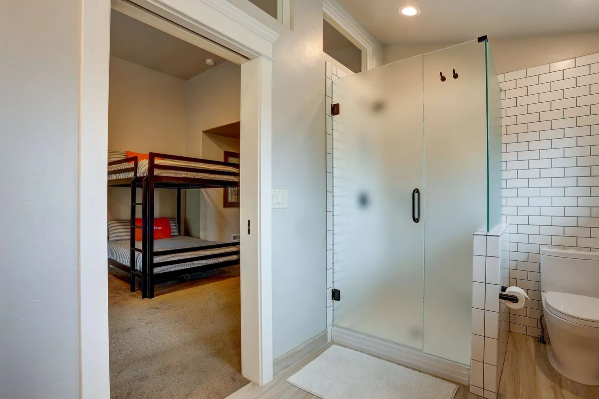 A multi-functional space with modern bunk beds, a glass shower in view, sleek tile work, and neutral wall colors. The area is both inviting and practical, suitable for morning routines or family bonding.