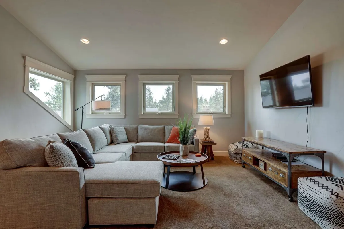 A cozy lower-level family room featuring a sectional sofa, coffee table, television, lamp, and windows providing natural light. The setup invites relaxation and group activities, with ample seating and a warm, welcoming vibe.