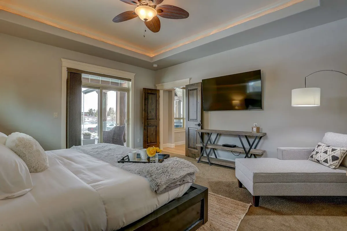 A tranquil bedroom with plush bedding on the bed, a large window streaming with natural light, a comfortable armchair for reading, and a decorative TV on a dresser. The scene exudes serenity and relaxation, perfect for unwinding after a busy day.